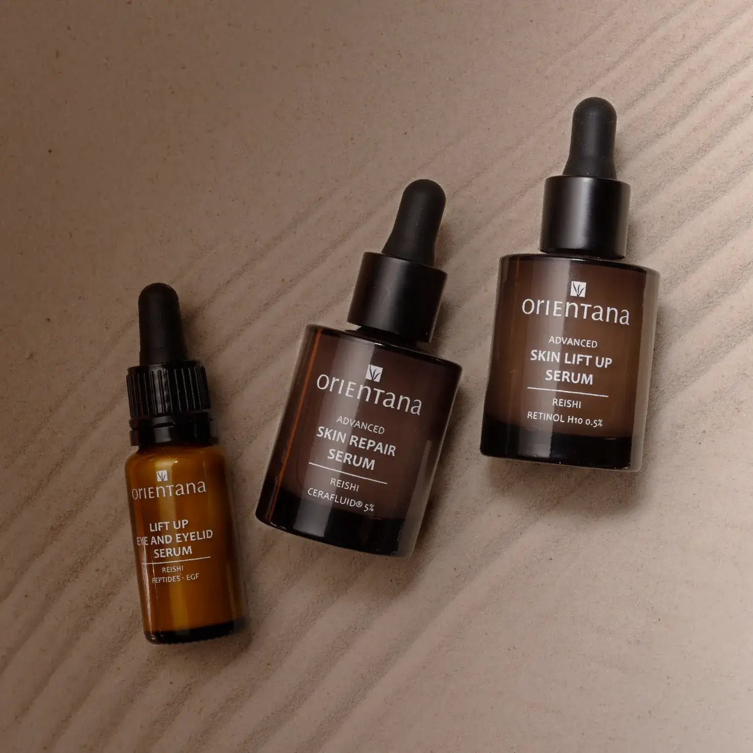 Trzy sera do twarzy Orientana z serii reishi i retinolem ustawione na jasnym tle: serum pod oczy Lift Up, Skin Repair Serum oraz Skin Lift Up Serum w szklanych butelkach z pipetami.
